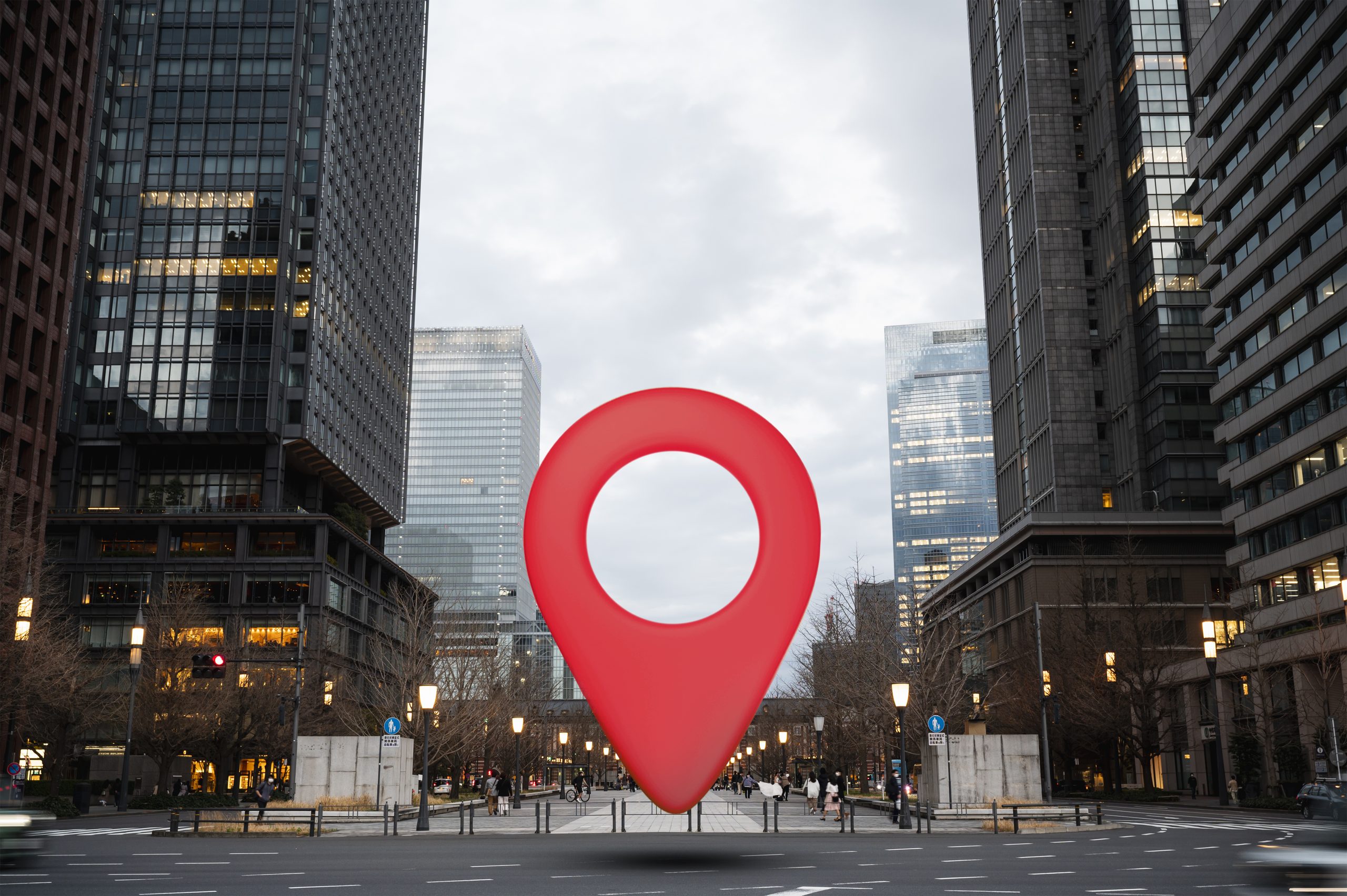 A imagem mostra um grande símbolo de localização em destaque, flutuando no meio de uma moderna rua urbana, rodeada por altos edifícios comerciais. O cenário transmite a ideia de um endereço comercial bem posicionado.